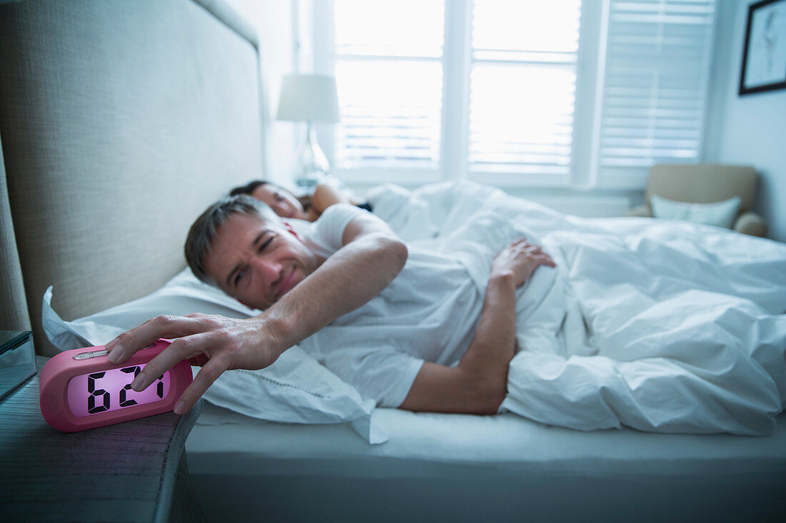 Man in bed turning off alarm clock