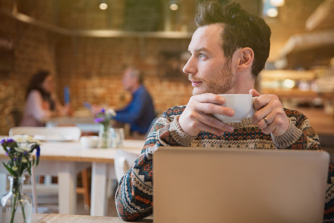 Pensive man drinking coffee at laptop