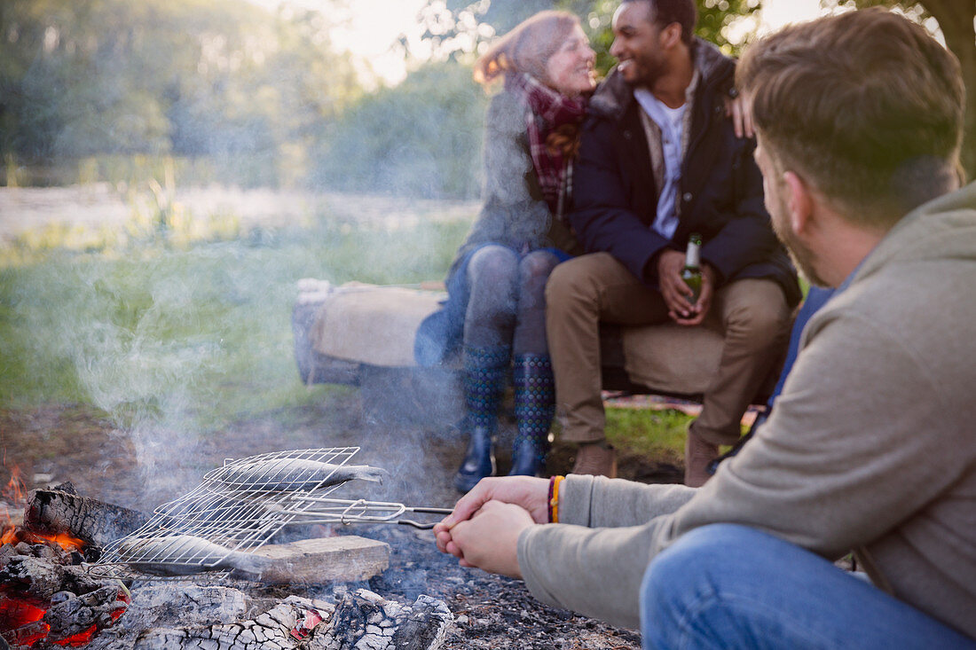 Friends cooking fish over campfire