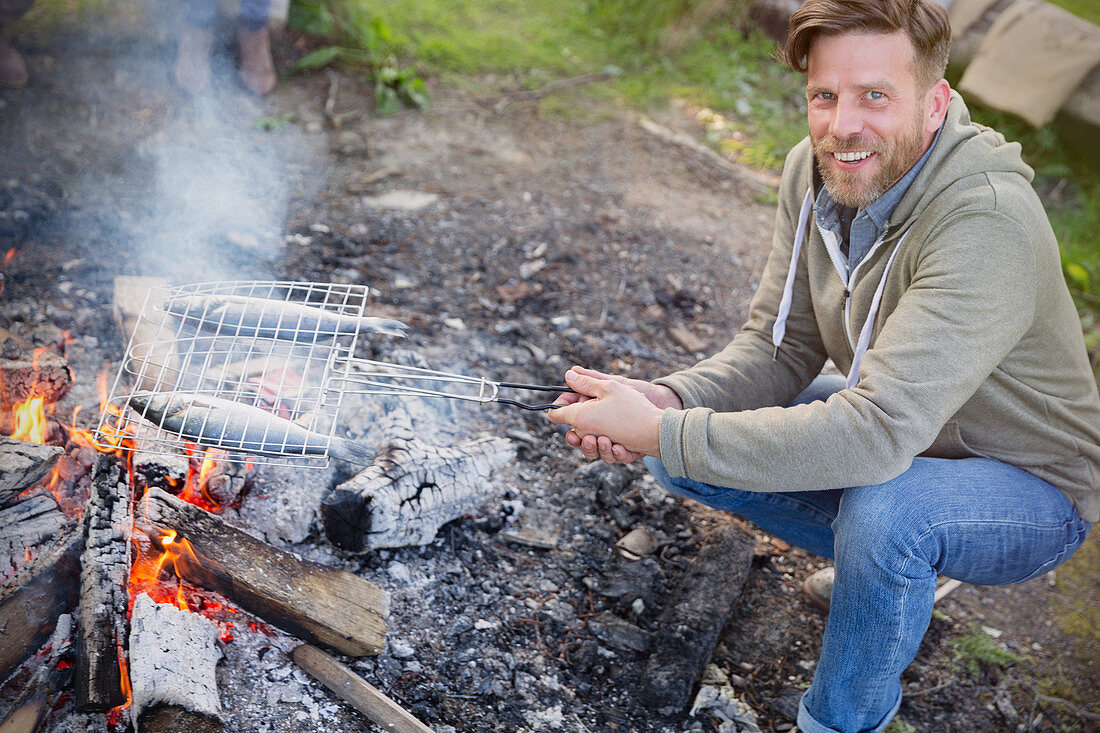 Smiling man cooking fish over campfire