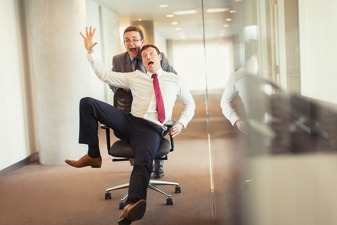 Businessman pushing colleague in office chair