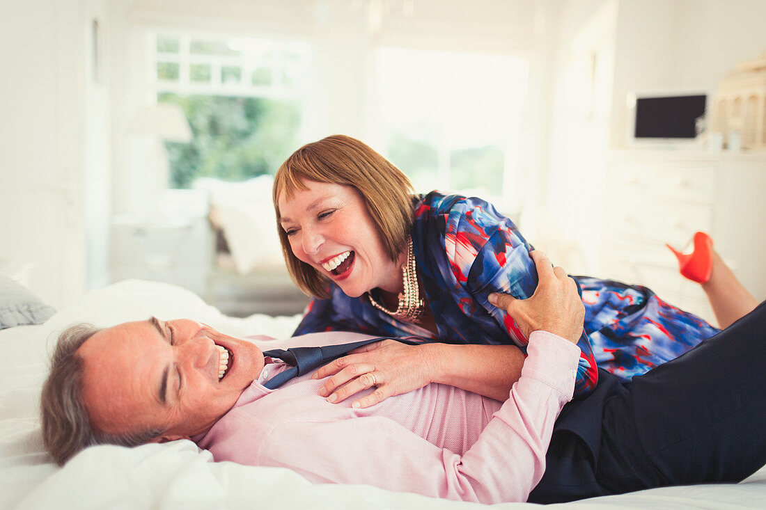 Well-dressed mature couple laughing on bed