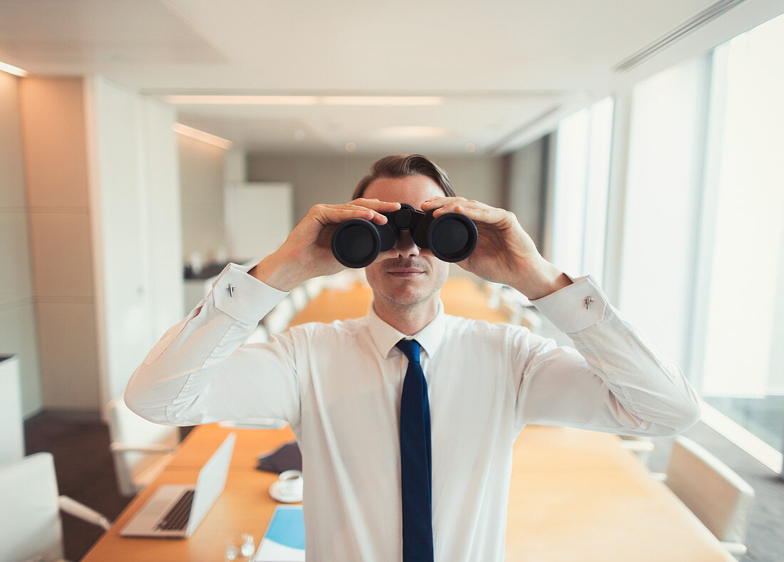 Businessman using binoculars in conference room