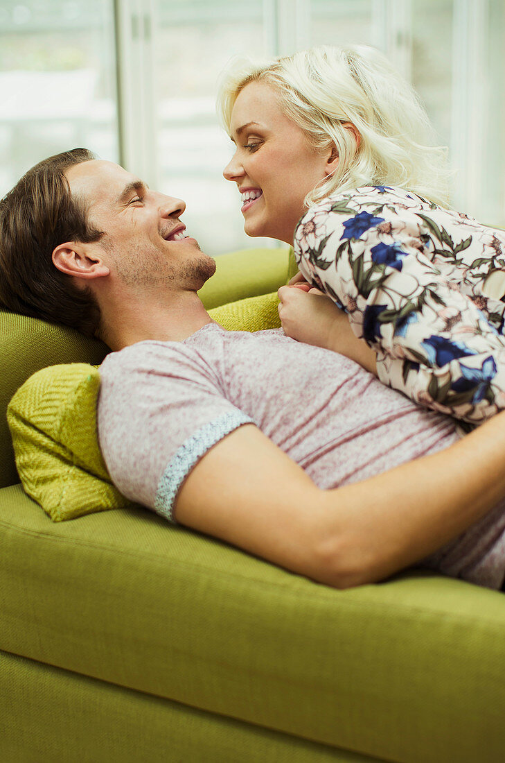 Affectionate couple laying on sofa face to face