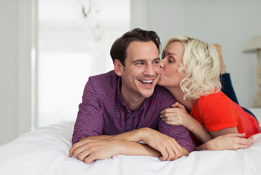 Affectionate wife kissing smiling husband on bed