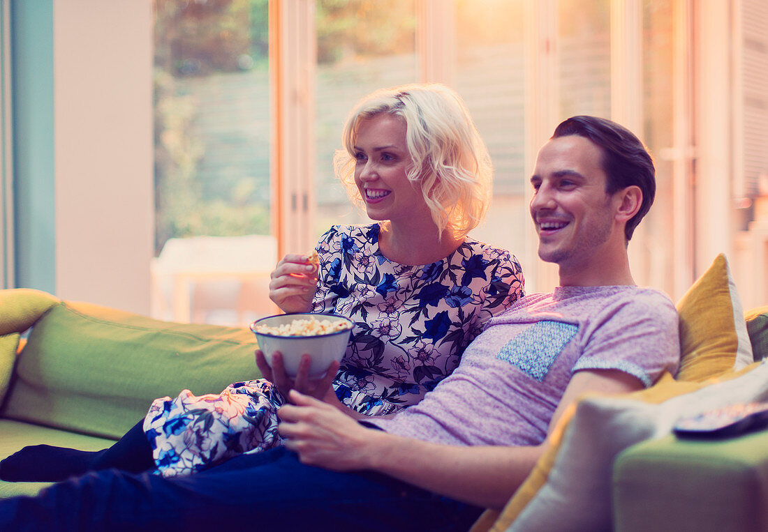 Couple watching TV and eating popcorn on sofa