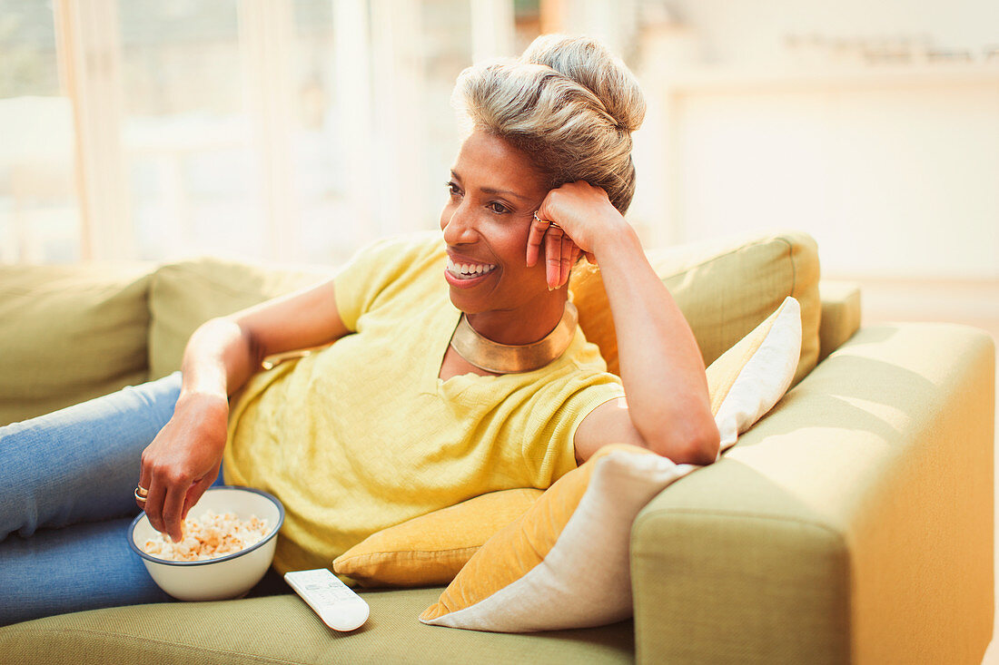 Mature woman watching TV and eating popcorn
