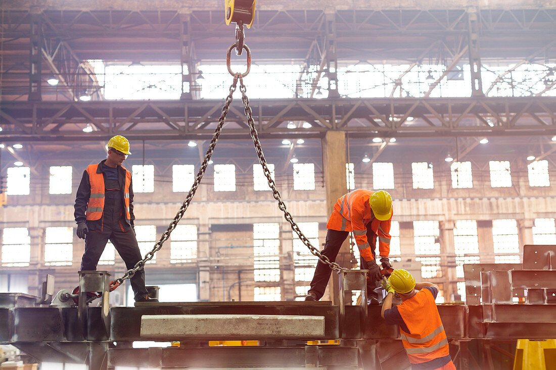 Steel workers fastening crane chain in factory