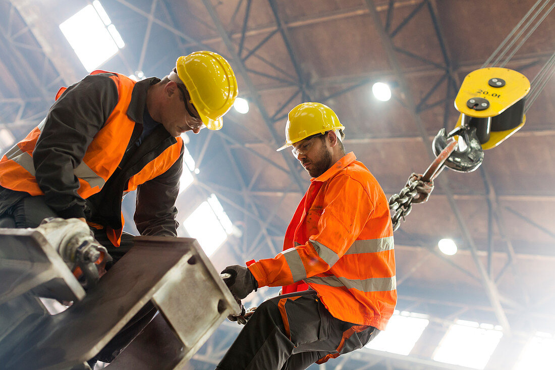 Steel workers fastening crane hook to steel