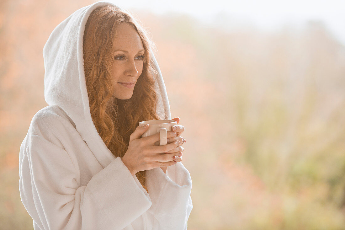 Serene woman in hooded bathrobe drinking coffee