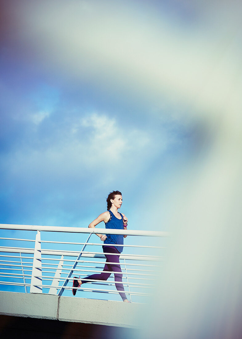 Female runner running on sunny footbridge