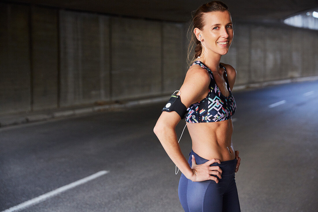 Portrait smiling fit female runner in urban tunnel