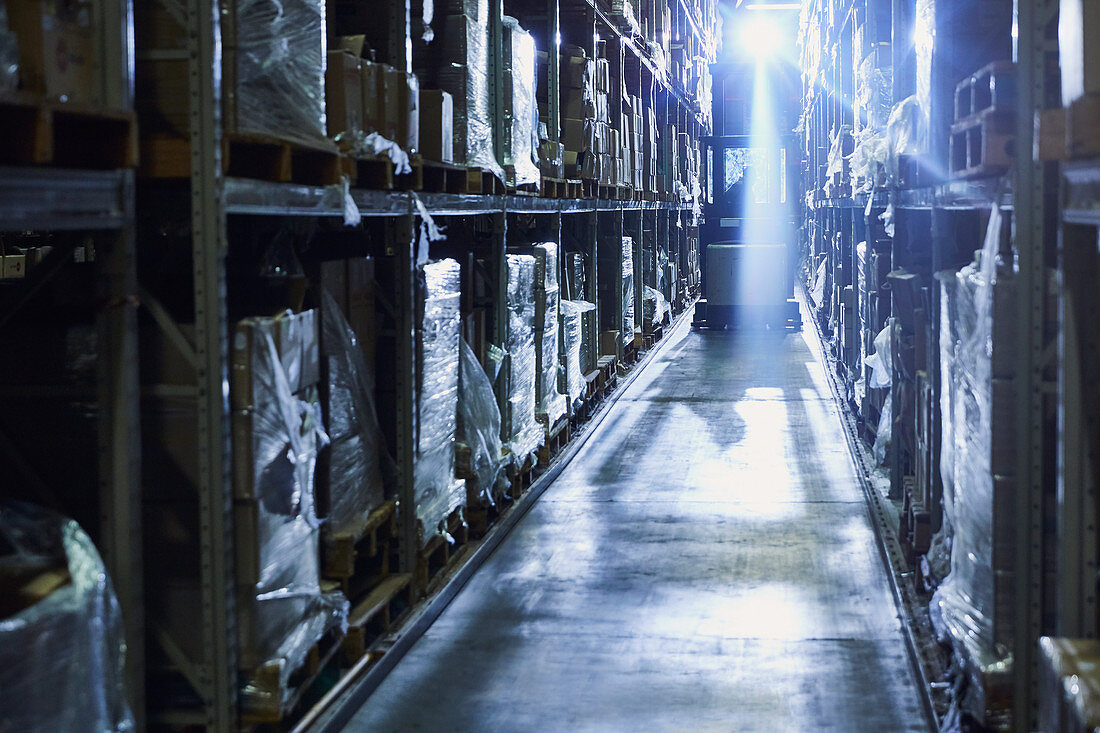 Back lit forklift in distribution warehouse aisle