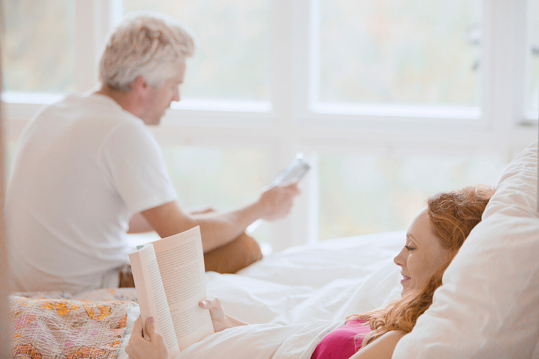 Couple reading book and digital tablet in bed