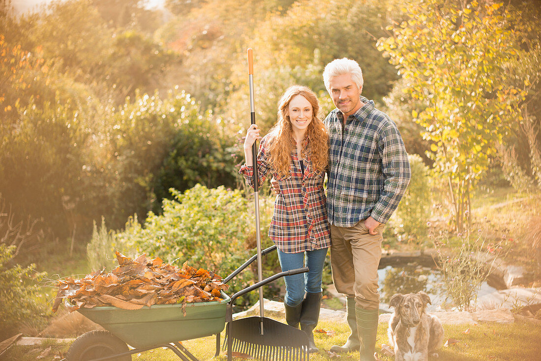 Portrait smiling couple with dog raking leaves