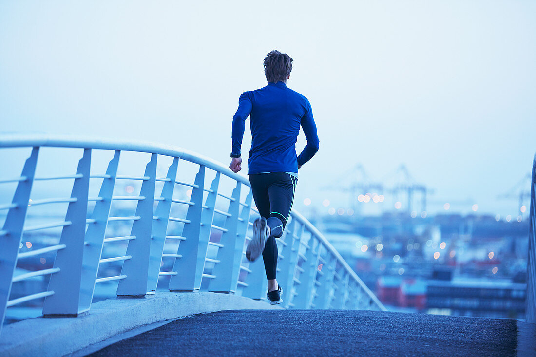 Male runner running on urban footbridge at dawn