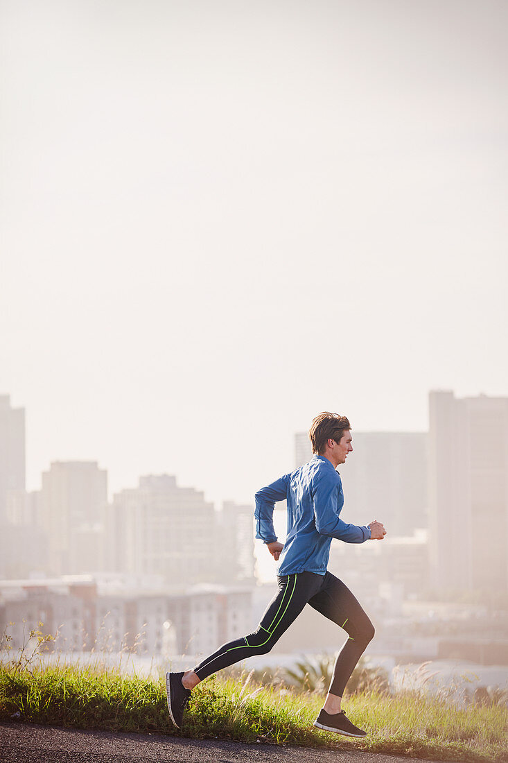 Male runner running on sunny urban city street