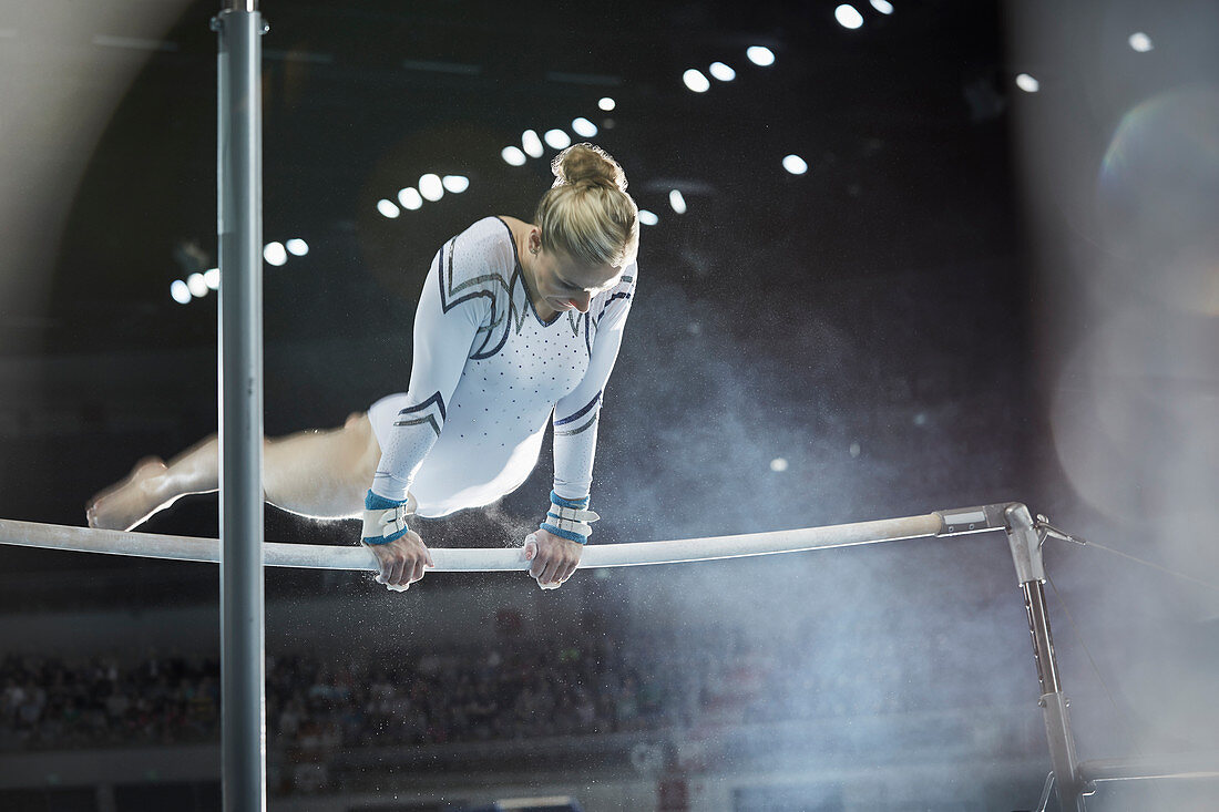 Female gymnast performing on uneven bars in arena