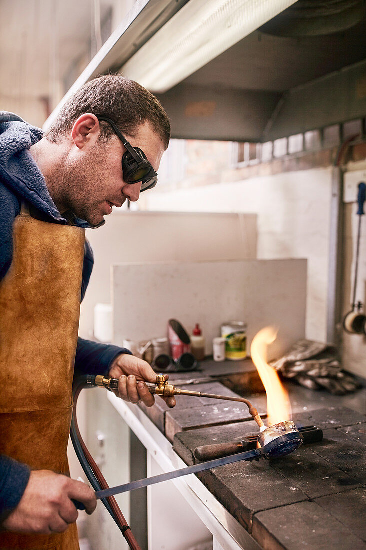 Jeweller heating metal using torch in workshop