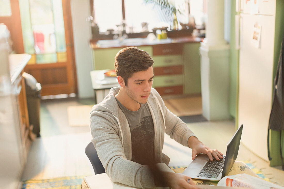 Young man college student studying in kitchen