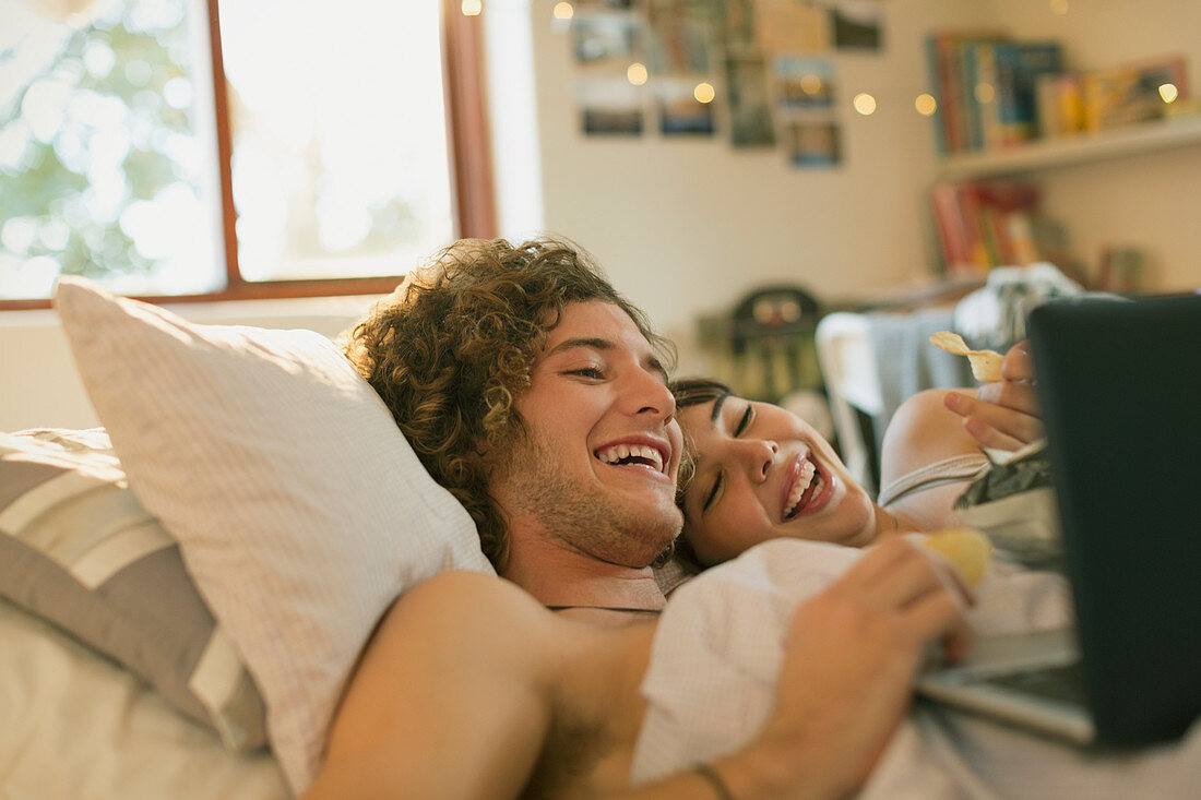 Smiling young couple laying in bed using laptop