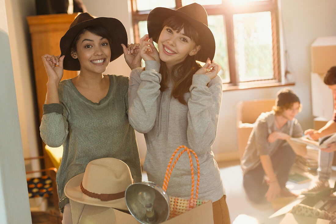 Women friends trying on hats moving into apartment