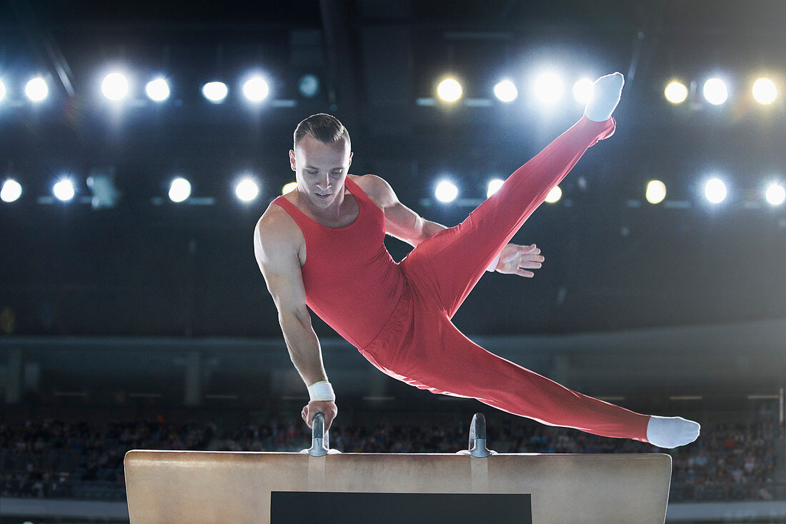 Male gymnast performing on pommel horse in arena