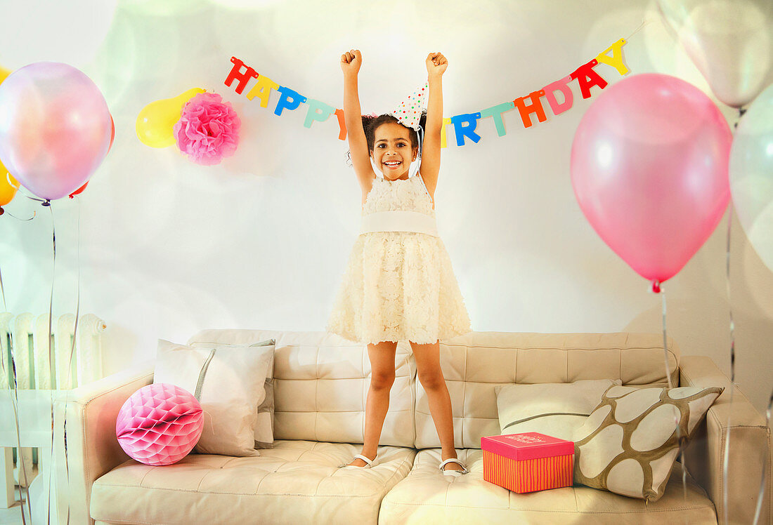 Girl with arms raised on sofa at birthday party