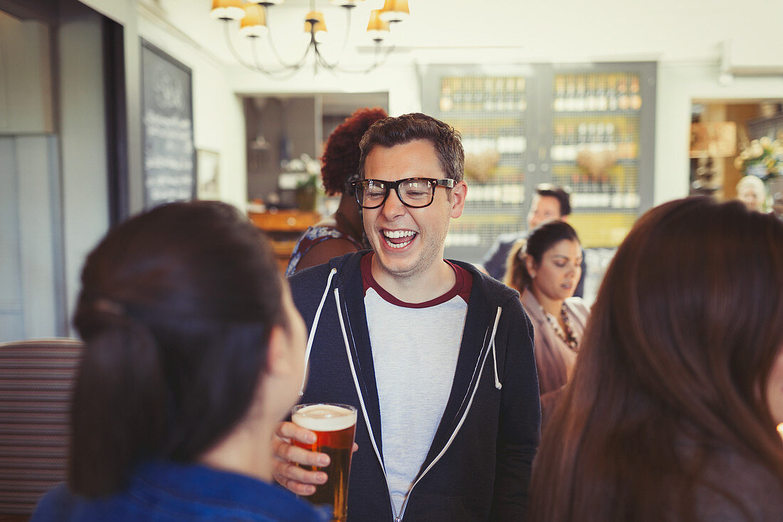 Man laughing and drinking beer with friends at bar