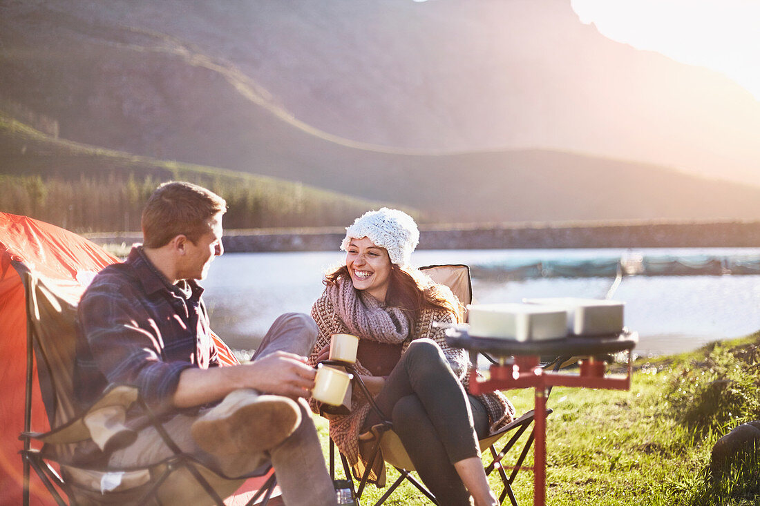 Young couple drinking coffee at lakeside campsite