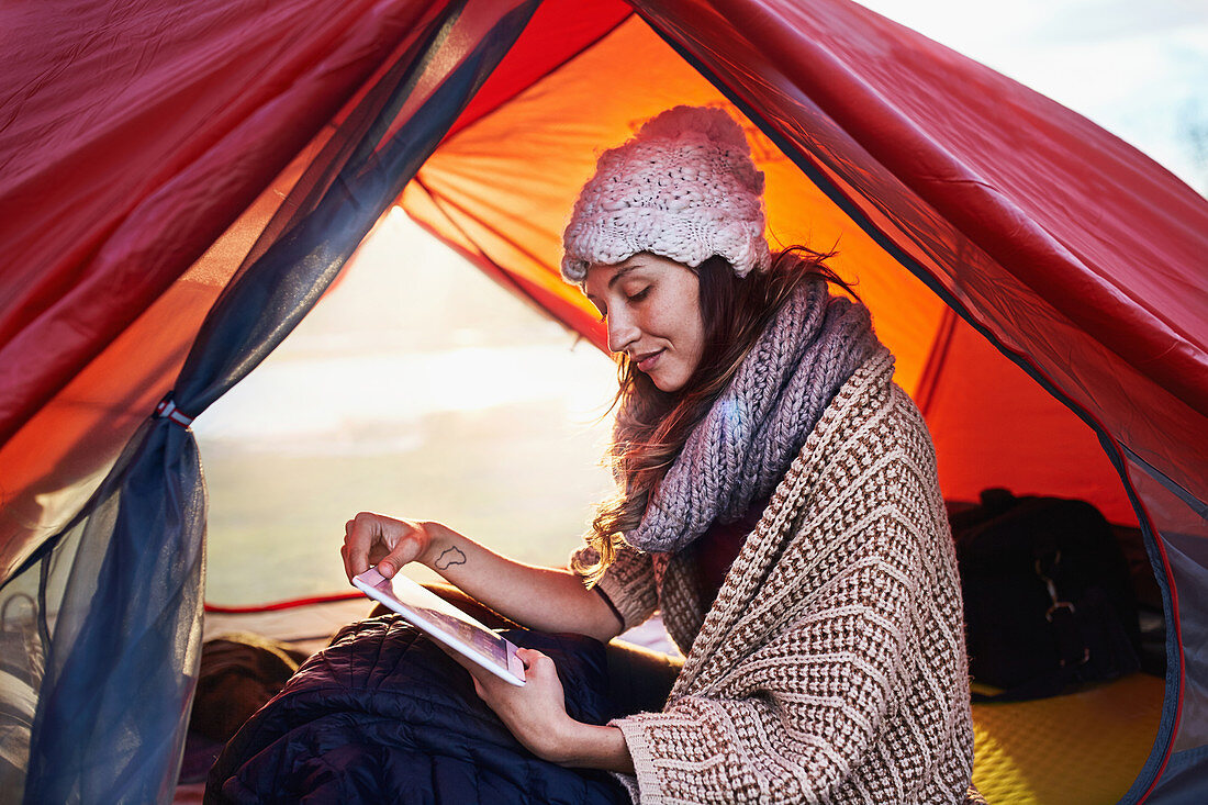 Young woman camping, using tablet in tent