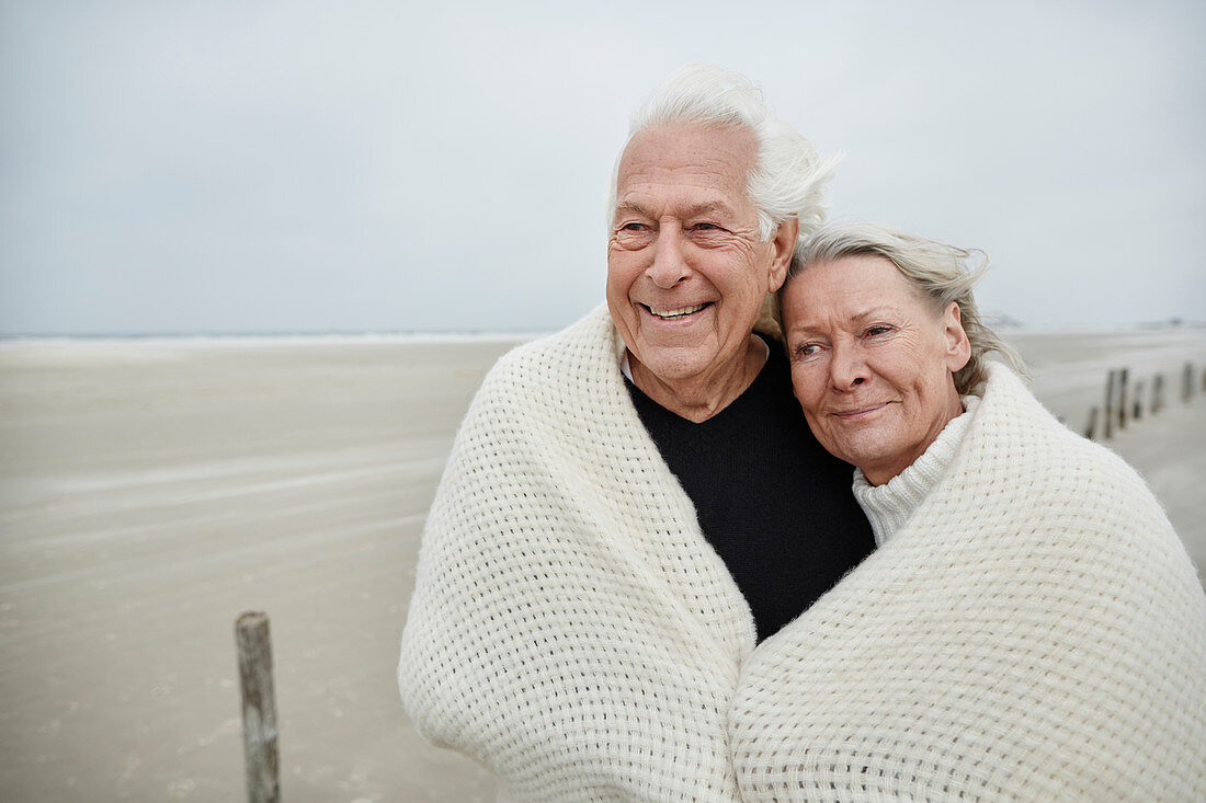 Senior couple wrapped in a blanket on beach