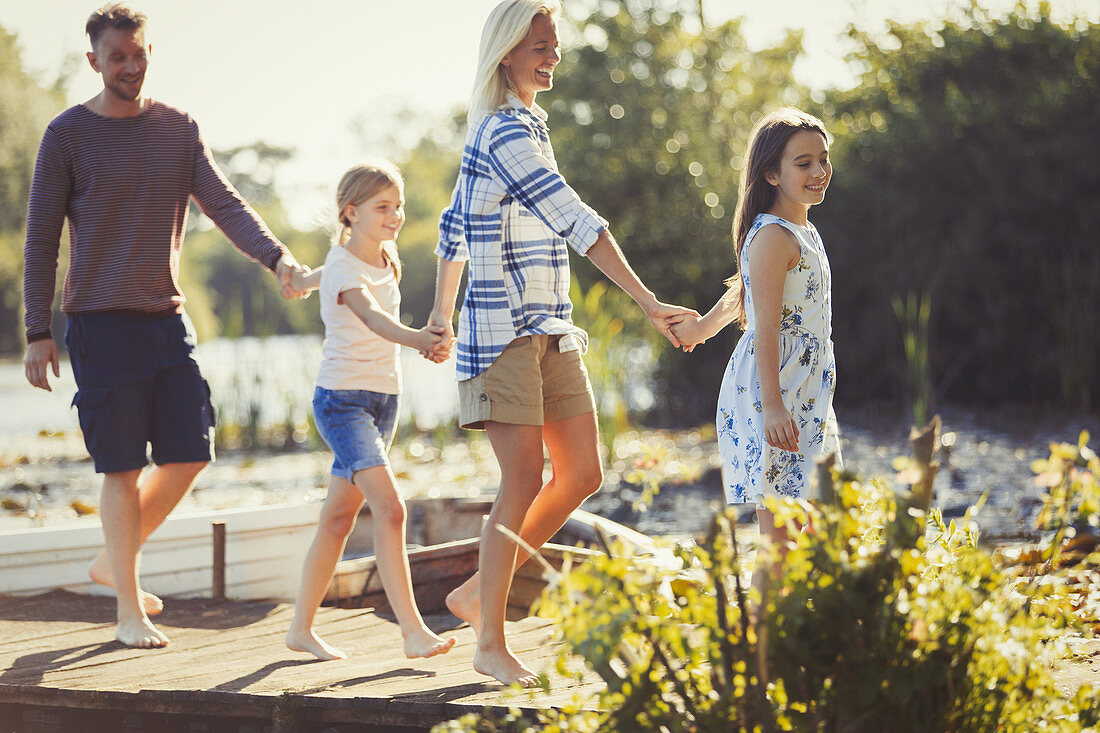 Barefoot family holding hands and walking on dock