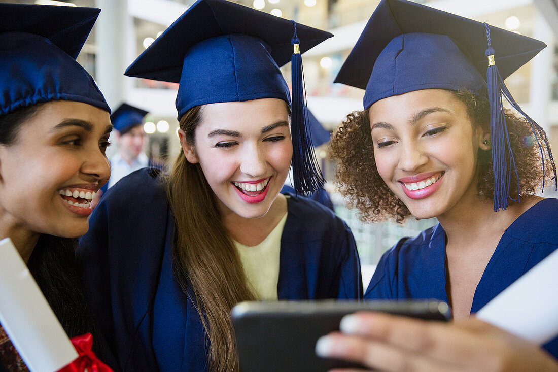 College graduates in cap and gown using cell phone