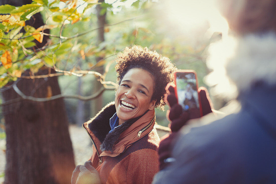 Smiling woman posing for boyfriend in autumn woods