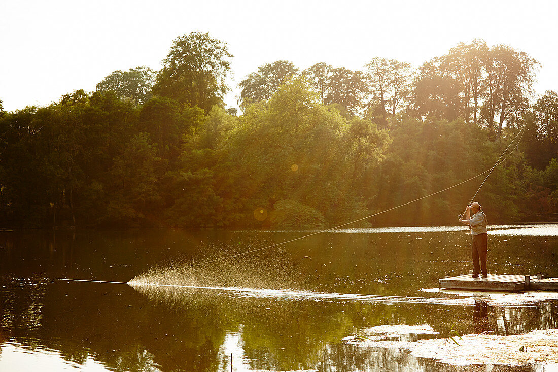 Senior man fly fishing on summer lake