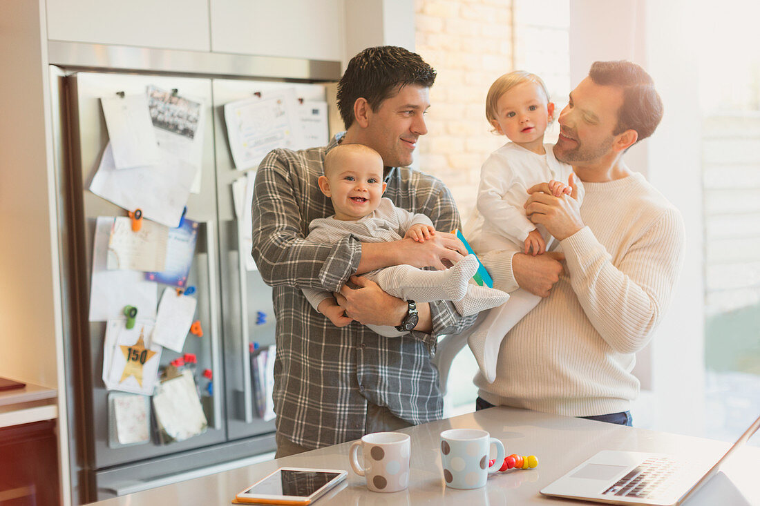 Male gay parents holding baby sons