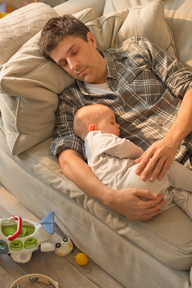 Exhausted father and baby son sleeping on sofa