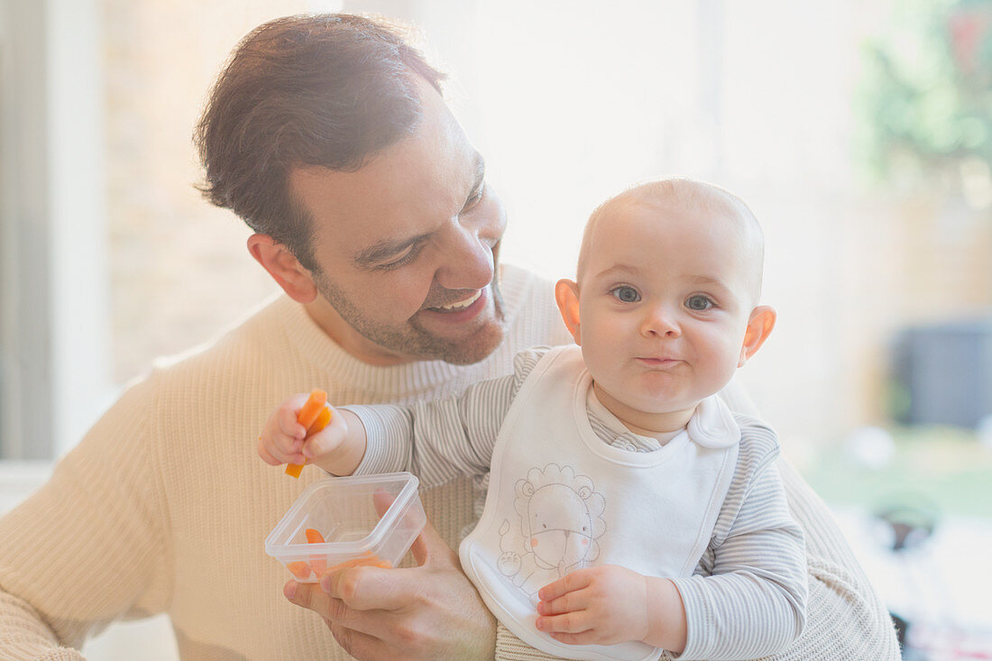 Portrait baby son and father eating carrots