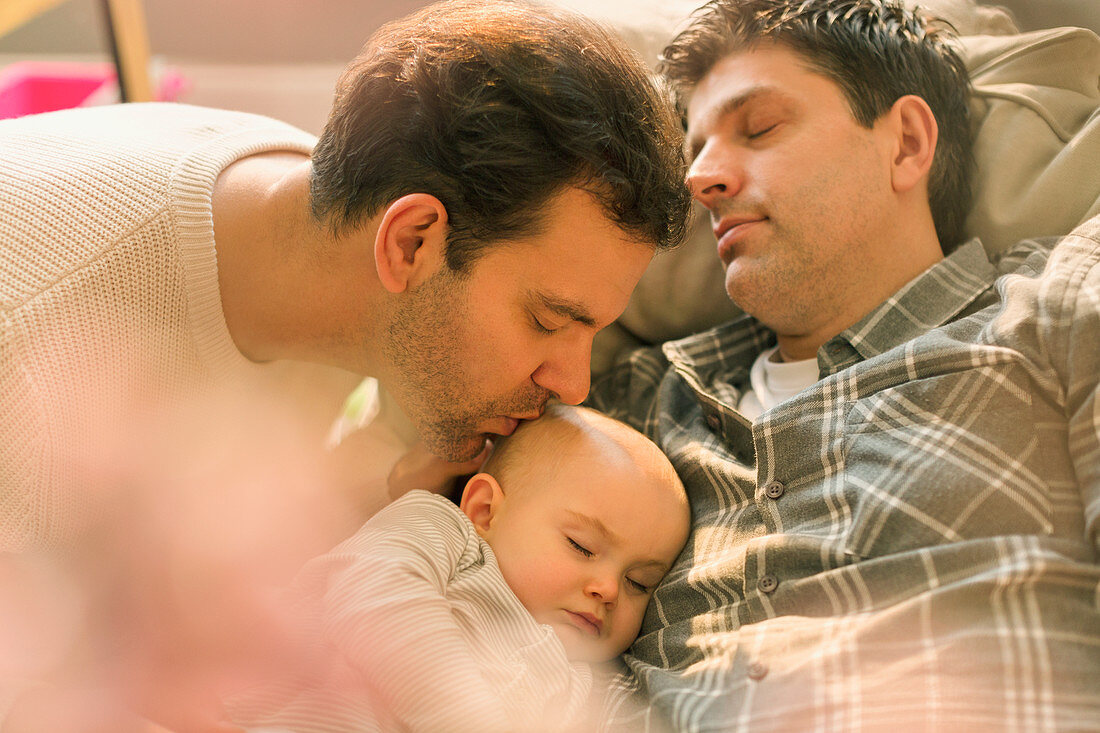 Affectionate male gay parents kissing baby son