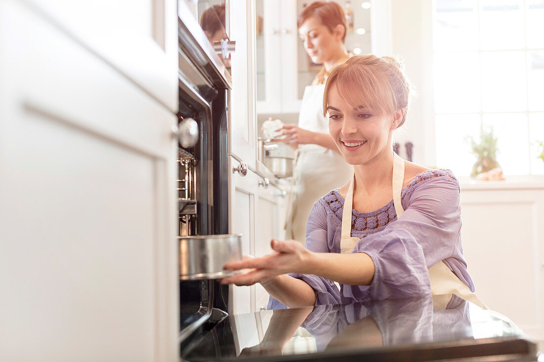 Smiling woman baking, placing cake in oven