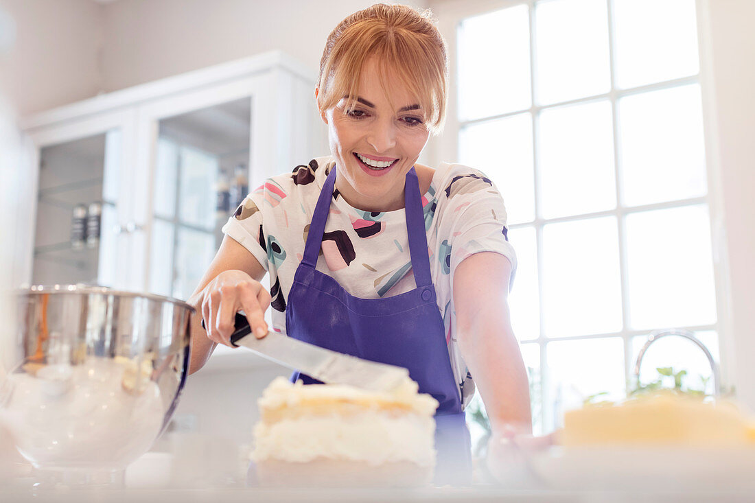 Smiling woman baking, icing layer cake