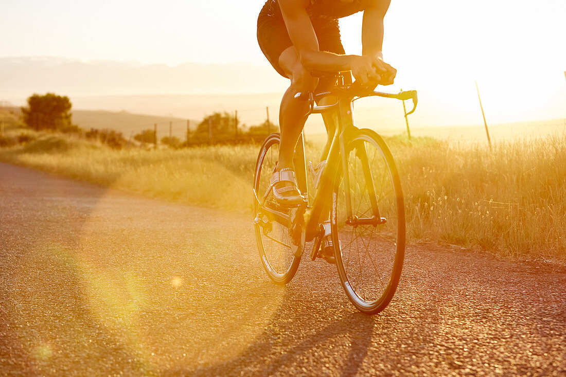 Male cyclist riding bike on sunrise rural road