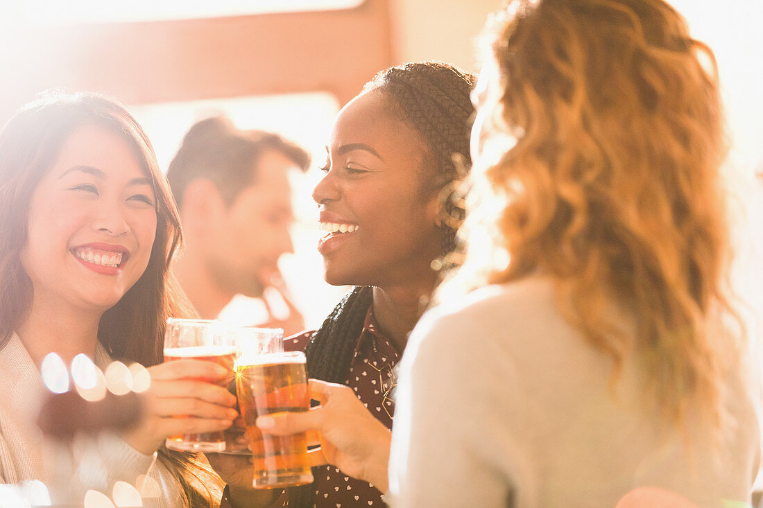 Smiling women friends toasting beer glasses in bar