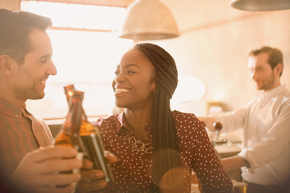 Smiling couple toasting beer bottles in bar