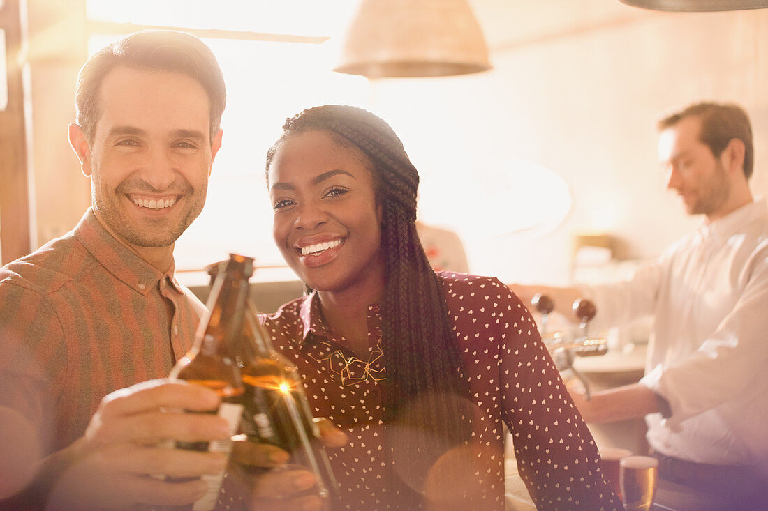 Portrait couple toasting beer bottles in bar