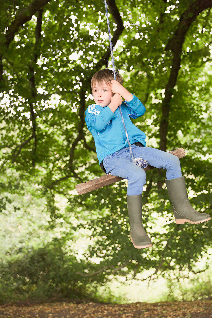 Boy in wellies swinging on tree rope swing
