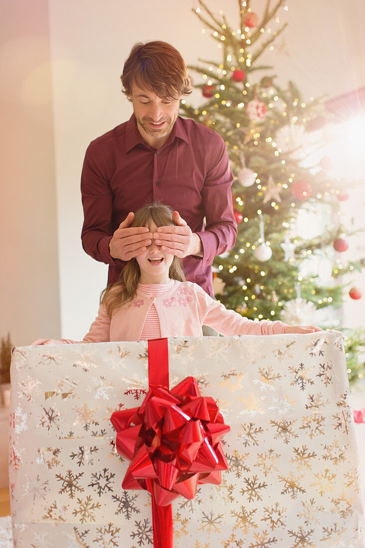 Father covering eyes of daughter holding gift