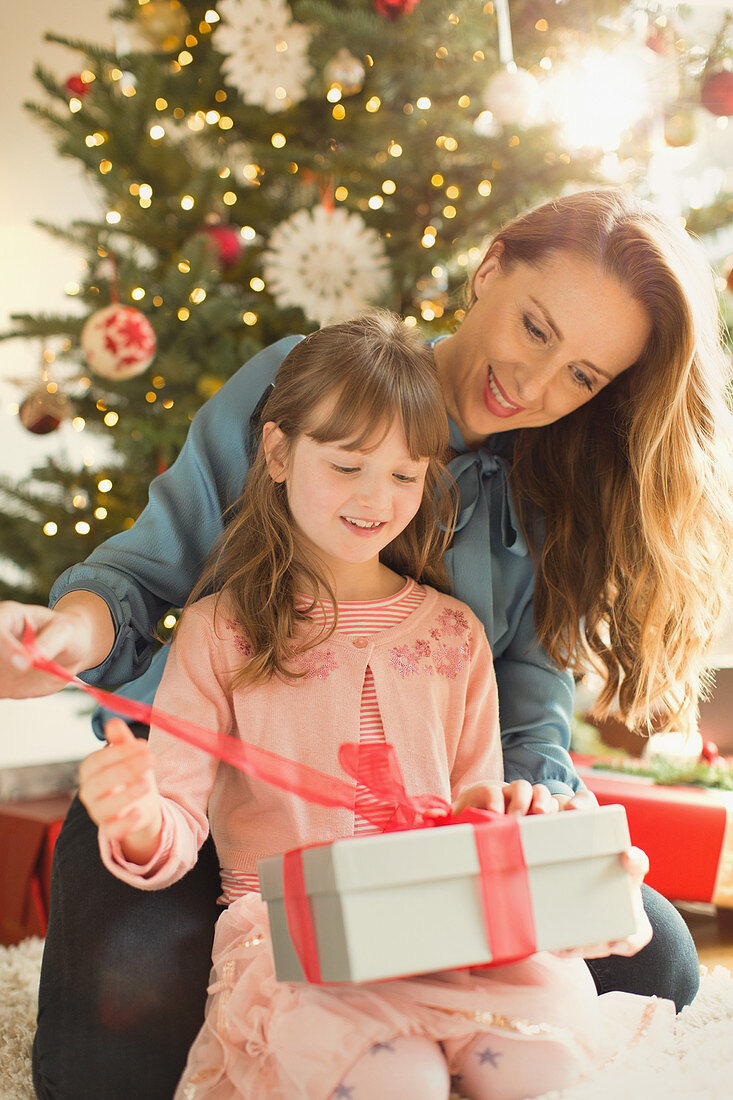 Mother helping daughter open Christmas gift