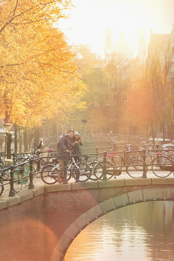 Young couple with bicycles taking selfie on bridge